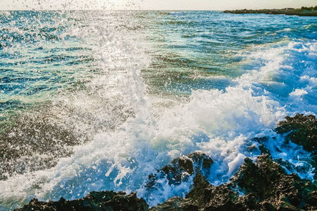 splashing waves crashing on the rocky shore at dawn sunの写真素材