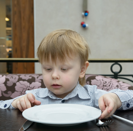 malnnnky boy sitting at a table with an empty plate waitingの写真素材