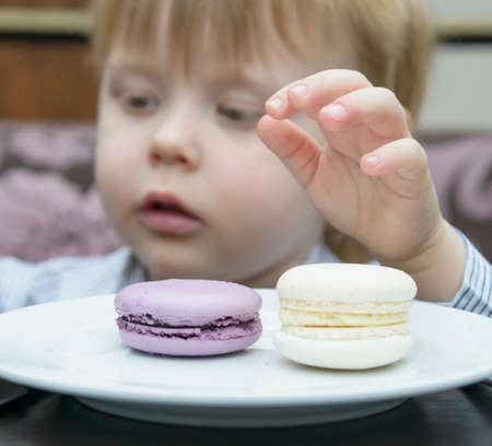 little blond boy sitting at a table eating cakeの写真素材