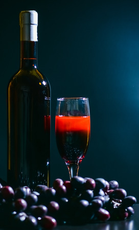 bottle of wine with a glass on a dark background with a bunch of grapesの写真素材