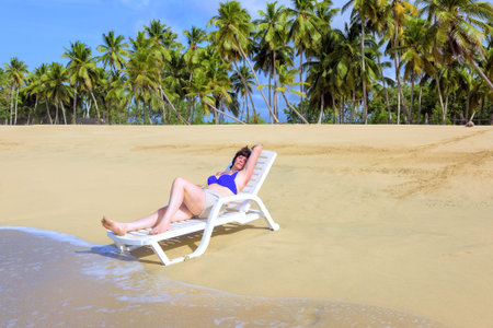 brown-haired, middle-aged woman lying on a lounger by the ocean shore