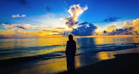 silhouette of a woman meets sunrise on the beach background palm treesの写真素材
