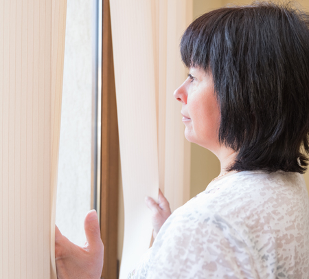 Brunette middle-aged woman is looking out the windowの写真素材