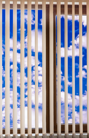 closed plastic blinds on the window with the reflection in the glass cloud skyの写真素材