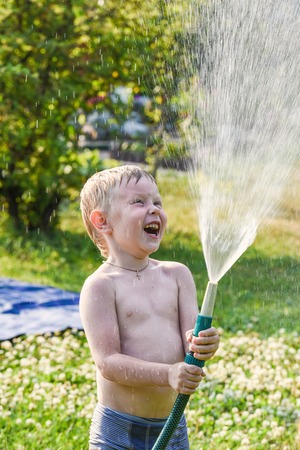 little blond boy pours water from a hose in the garden plantの写真素材