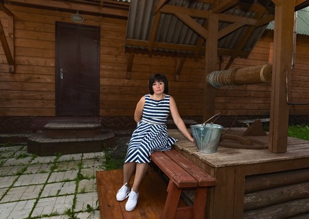 middle-aged brunette woman standing at the village well with a wooden bucketの写真素材