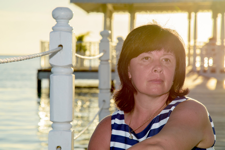 brunette woman of average years striped dress at sunset on the seashoreの写真素材