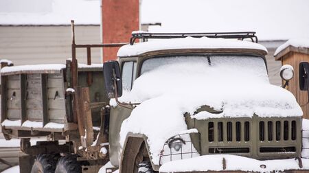 battered old car abandoned covered with snow in winterの写真素材