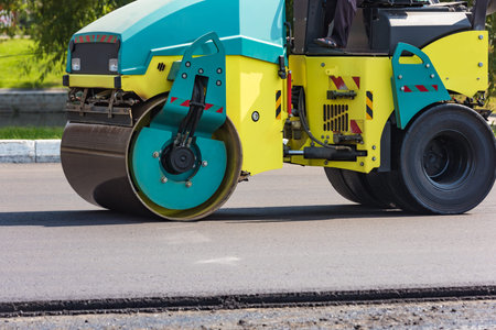 Roller machine rolls fresh laid asphalt on the road in the city