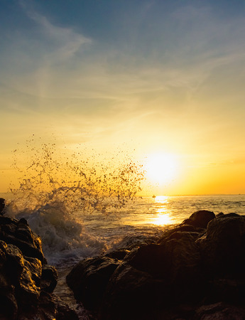 Morning dawn on the seashore waves crash against the rocks splashing water against the sunの写真素材