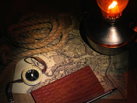 planning a trip at night at a table in the light of a kerosene lamp. Researching an old map with a compass and writing to notebookの写真素材
