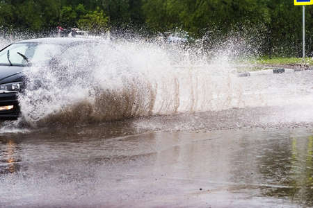 Russia. Moscow.May 30, 2020 . A car drives through a pool of water with splashes. Spring flood in the city.のeditorial素材