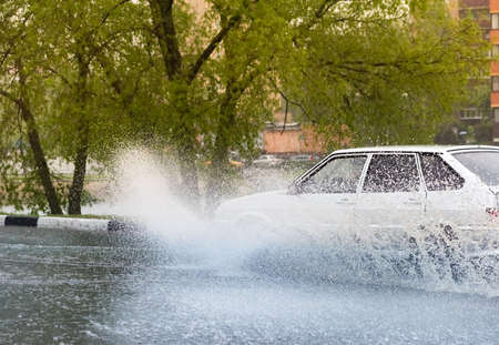 Russia. Moscow.May 30, 2020 . A car drives through a pool of water with splashes. Spring flood in the city.のeditorial素材