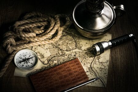 Preparing for an adventure trip. At night, inspection of an old map with a compass and a magnifier under the light of a lamp. Dark background.の写真素材