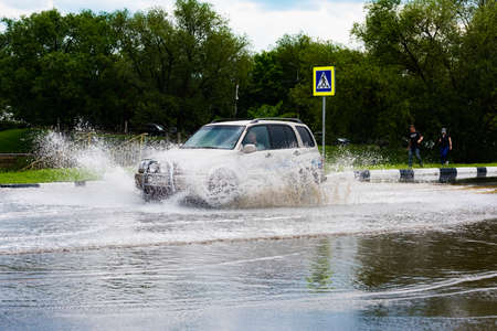 Russia. Moscow.May 30, 2020. A car drives through a pool of water with splashes. Spring flood in the city.のeditorial素材