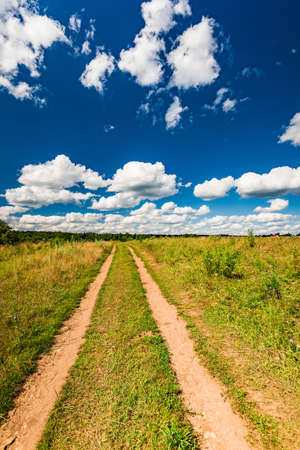 rural landscape dirt road in the field blue sky with white cloudsの写真素材