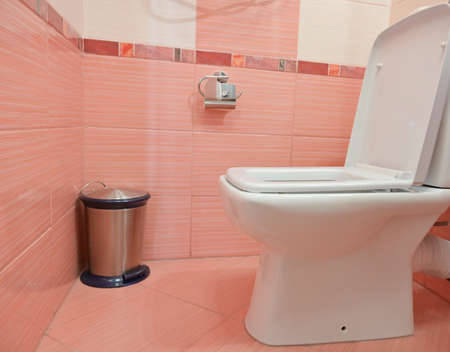 white tiled toilet bowl and trash can in the washroom with pink tilesの写真素材