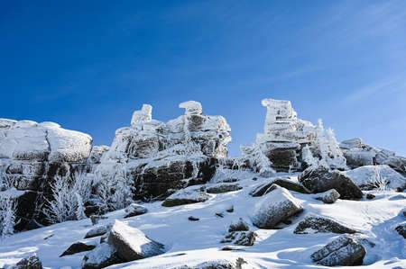 stone rock in winter frost covered with snow on blue sky backgroundの写真素材