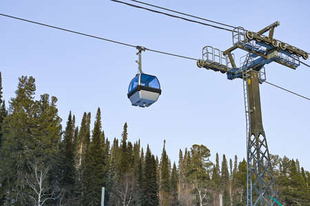 Chair ski lift for mountain skiers and snowboarders moves in the air on a rope on the background of winter snow capped mountains.の写真素材