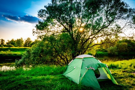 green tourist tent in nature on the banks of the river at sunsetの写真素材