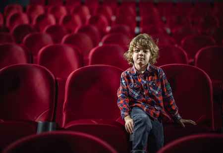 little boy at the cinema in an empty auditorium on a red armchairの写真素材