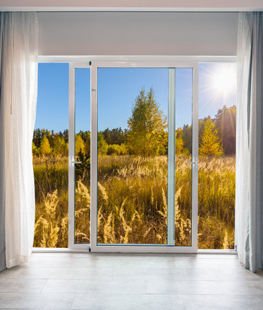 view through an open glass door on a sunny autumn landscapeの写真素材