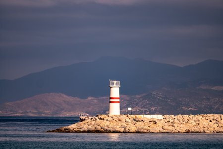 Small passenger ferry ship sails near white lighthouse tower on a dayの写真素材