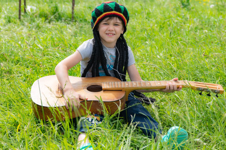 punk boy with dreadlocks and guitar sitting on the grassの写真素材