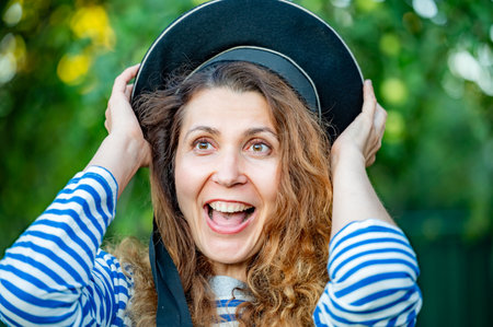 portrait of a young curly woman with red hair in a navy vest and capless capの写真素材