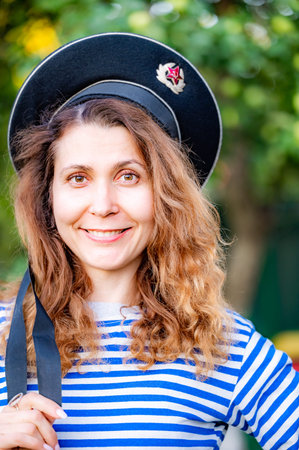 portrait of a young curly woman with red hair in a navy vest and capless cap