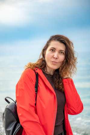 young woman in a red jacket enjoying a sunny day on the seashore