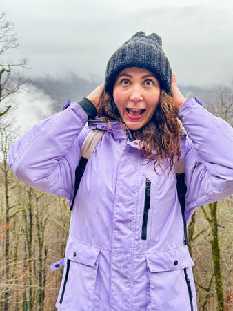 Happy young caucasian woman in jacket enjoying walk under snowfall in winter forest
