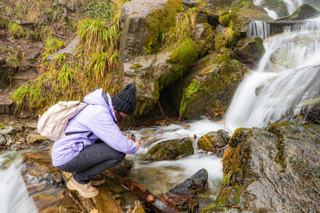 Curly woman looking on waterfall in . View from the back, wind in hair, cloudy weatherの写真素材