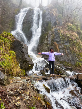 Curly woman looking on waterfall in . View from the back, wind in hair, cloudy weatherの写真素材