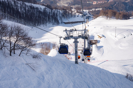 ski lift gondolas against blue sky over slope at ski resort on sunny winter dayの写真素材