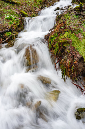 Icy water from snowmelt rushes through a mountain gorge between bouldersの写真素材