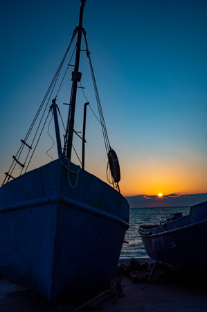 Two boats are sitting on the beach at sunset. The sky is a beautiful mix of orange and blue huesの写真素材