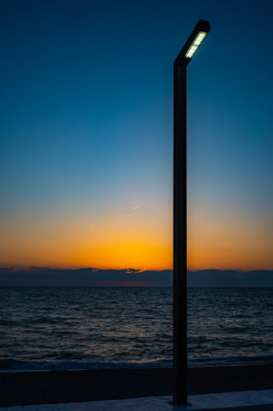 The sun is setting over the ocean, casting a warm glow on the water. The sky is a deep blue, with no clouds in sight. The beach is empty, with only the sound of the waves crashing against the shoreの写真素材