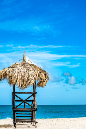 A beach hut with a straw roof sits on the beach. The hut is empty and the beach is calmの写真素材