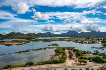 A beautiful view of a large body of water with a clear blue sky and white clouds. The sun is shining brightly, and there are mountains in the distance.の写真素材