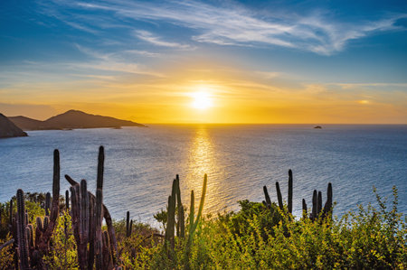 The image captures a stunning sunset over the ocean, with the sun setting in the distance. The sky is filled with clouds, creating a beautiful and serene atmosphere. In the foregroundの写真素材
