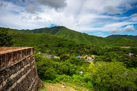 A lush green mountain range with a small town in the valley below. The sky is clear and the sun is shiningの写真素材