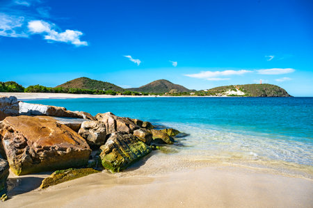 A beautiful beach with a blue ocean and a mountain in the background. The beach is empty and the water is calmの写真素材