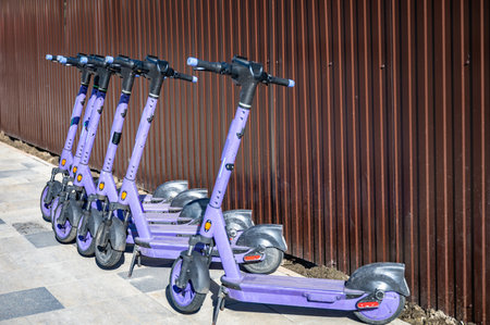 Five purple scooters are parked on a sidewalk against a brown corrugated metal wall.の写真素材
