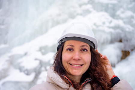 Woman wearing a white jacket and a helmet. She is smiling and holding her glasses. She is wearing a black strap on her shoulderの写真素材