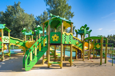 Park with a yellow fence and a variety of green play structures. The play structures include slides,...