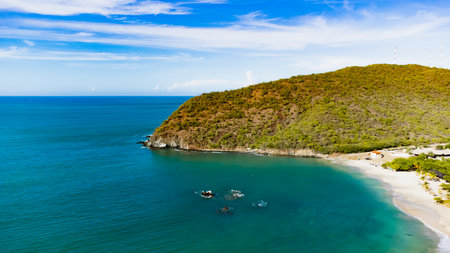 Stunning view of a tropical beach with turquoise water gently lapping the sandy shore. Mountains form a picturesque backdrop, creating a serene and idyllic coastal scene.の写真素材