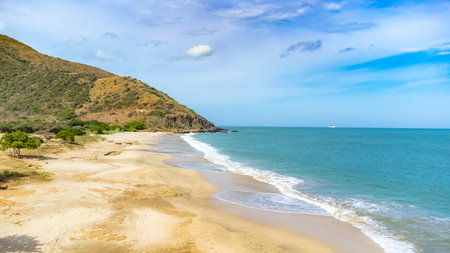 Calm ocean scene with a distant boat and lush hill under a vibrant blue sky. Gentle waves meet the sandy shore, creating a peaceful and serene atmosphere perfect for relaxation.の写真素材
