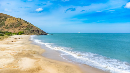 Calm ocean scene with a distant boat and lush hill under a vibrant blue sky. Gentle waves meet the sandy shore, creating a peaceful and serene atmosphere perfect for relaxation.の写真素材