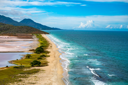 A breathtaking aerial view captures the vibrant salt flats alongside the pristine coastline and mountains of Venezuela. The vivid contrast between land and sea creates a stunning natural landscape.の写真素材